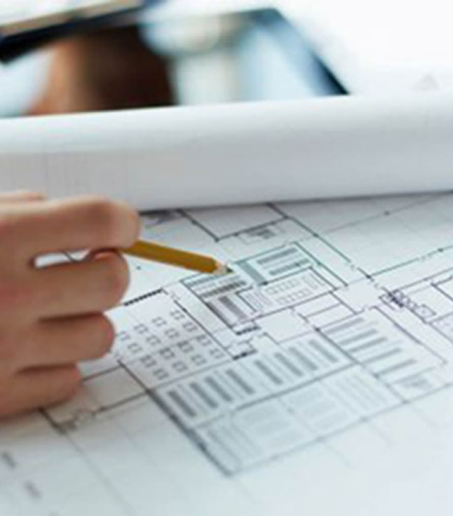A hand holding a pencil over architectural blueprints on a table.