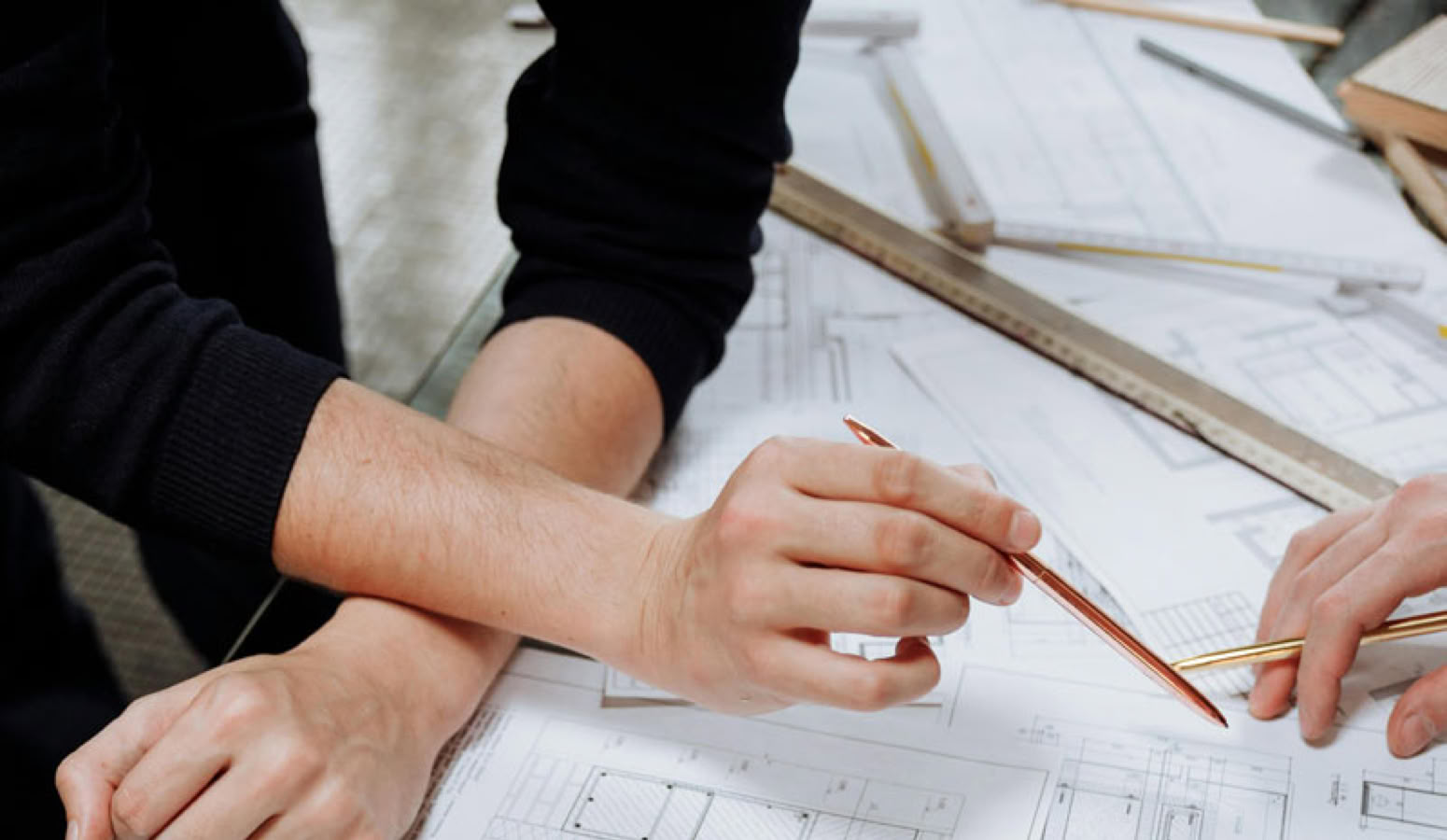 Hands of people working over architectural blueprints with a color palette and pencils on a table.