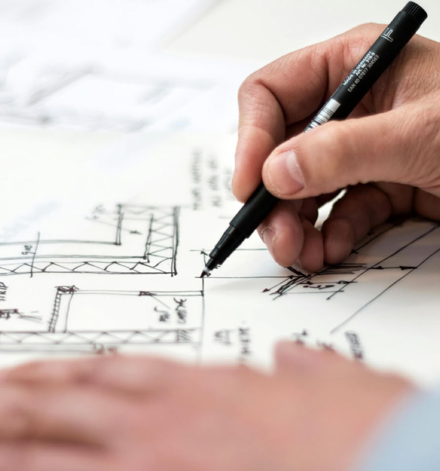 A person drawing architectural plans with a pen on a sheet of paper.